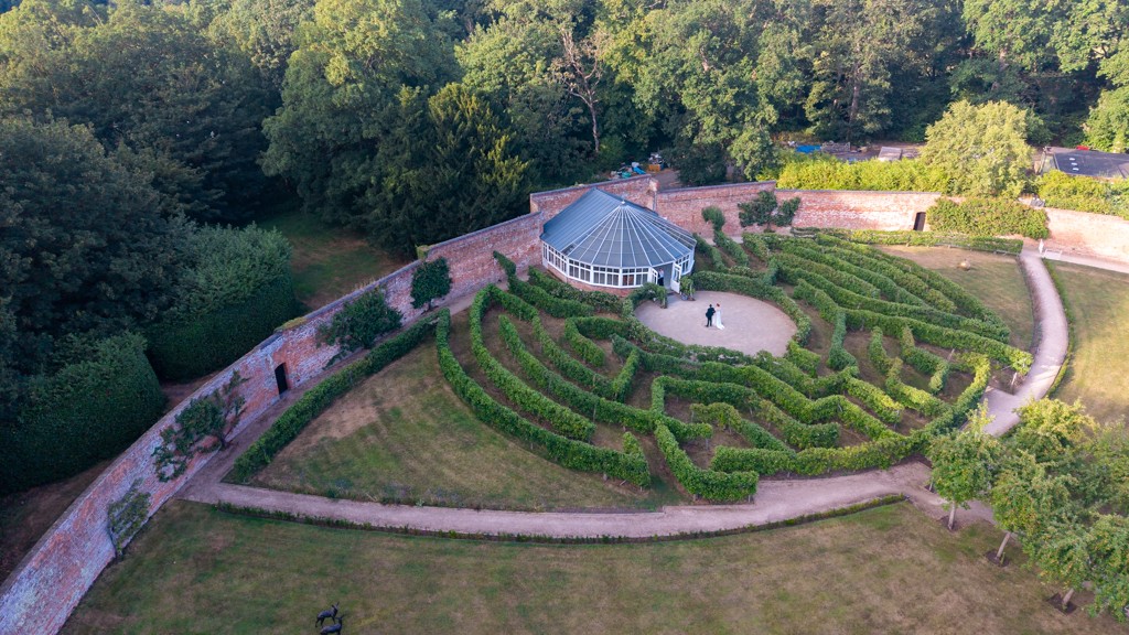 Aerial view of a couple walking through a manicured garden maze on their wedding day